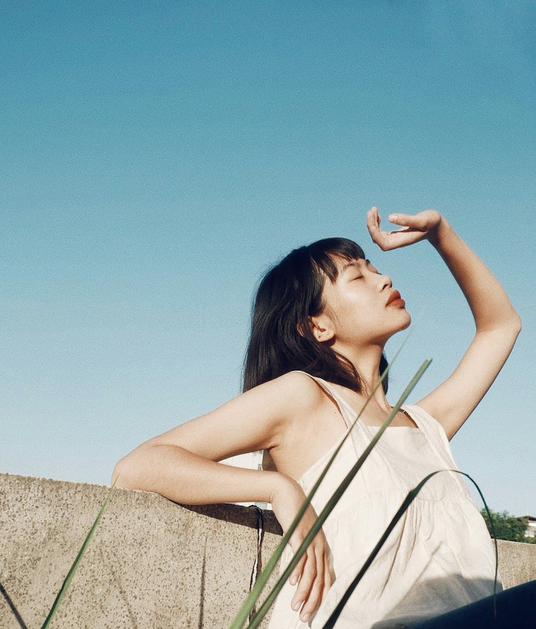 Model in a white camisole shading her eyes against a blue sky