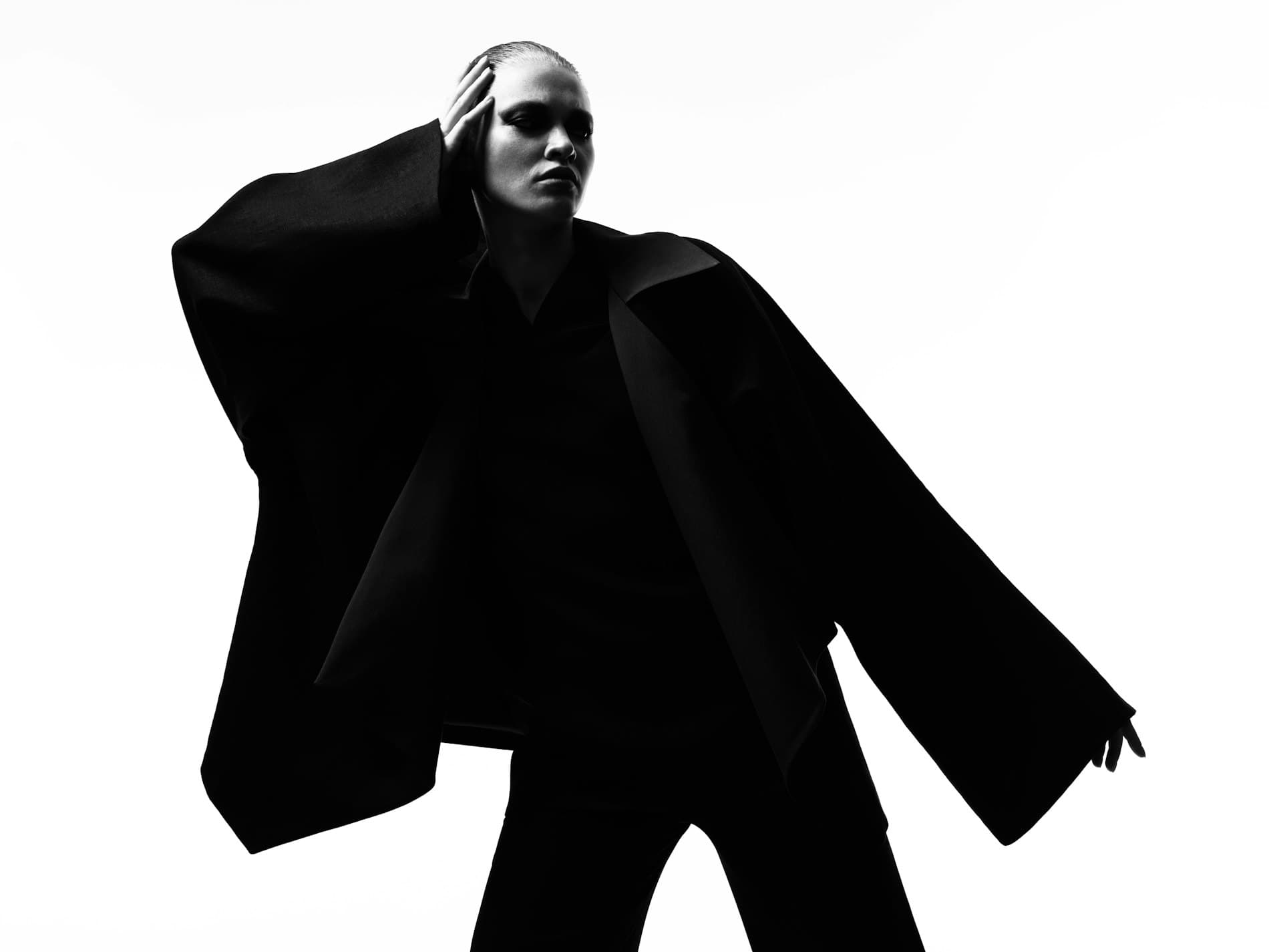 Model in an oversized black coat with one hand raised to her head